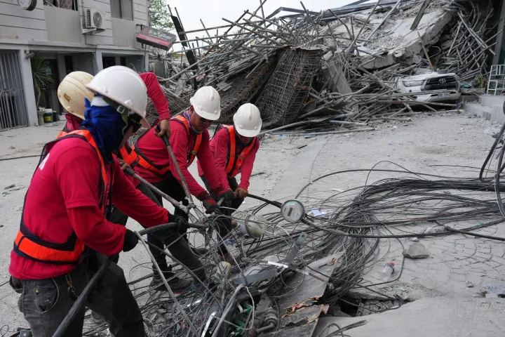 Workers cut cables during a search operation at a collapsed building 