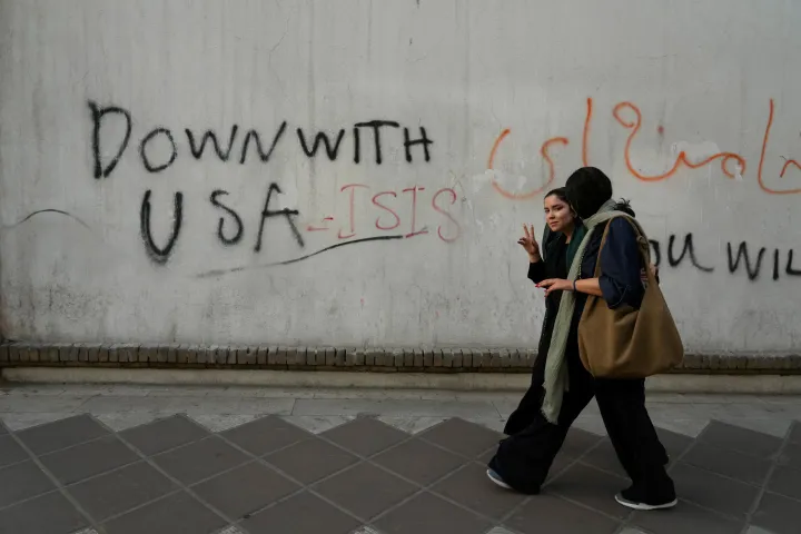 A woman reacts to the camera as she walks past an anti-U.S. graffiti painted on the wall of the British Embassy in Tehran, Iran