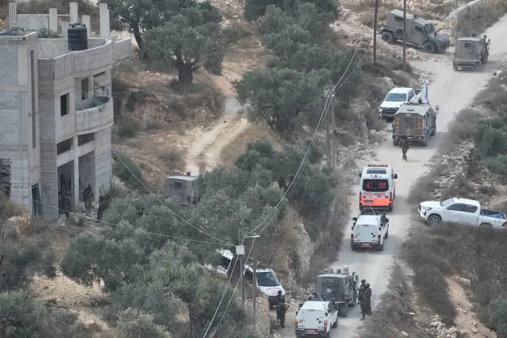 Israeli soldiers secure a building under construction as ambulances evacuate injured Palestinians following an attack by Israeli settlers in the occupied West Bank village of Qusra