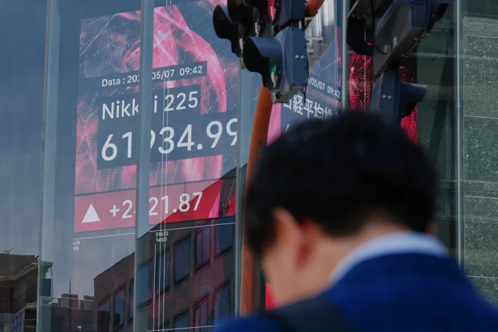 A person stands in front of an electronic stock board showing Japan's Nikkei index
