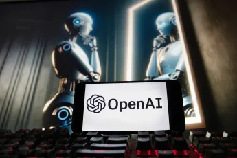Το λογότυπο της OpenAI εμφανίζεται σε κινητό τηλέφωνο, με μια εικόνα σε οθόνη υπολογιστή που δημιουργήθηκε από το μοντέλο μετατροπής κειμένου σε εικόνα Dall-E του ChatGPT.
